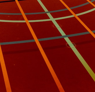 A sports court with intersecting lines in orange and blue, creating geometric patterns on a reddish-brown surface.
